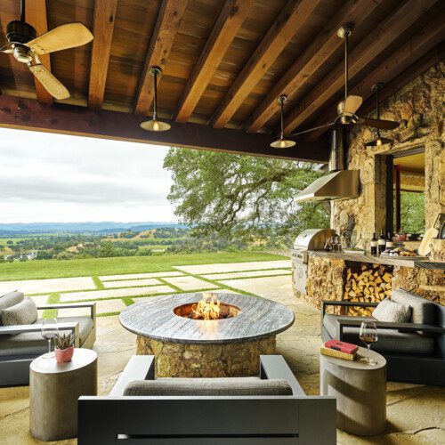 An outdoor fire pit and pizza oven tucked under deep eaves with a sweeping view beyond