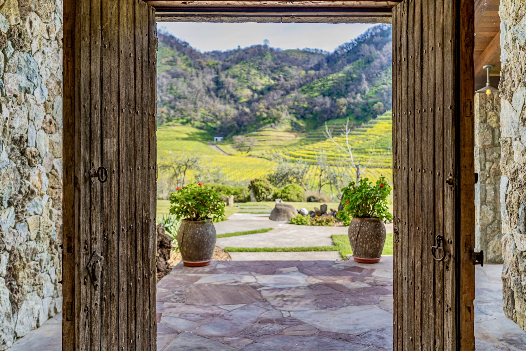A rustic door opens onto a stone patio with rugged hills and vineyards in the distance
