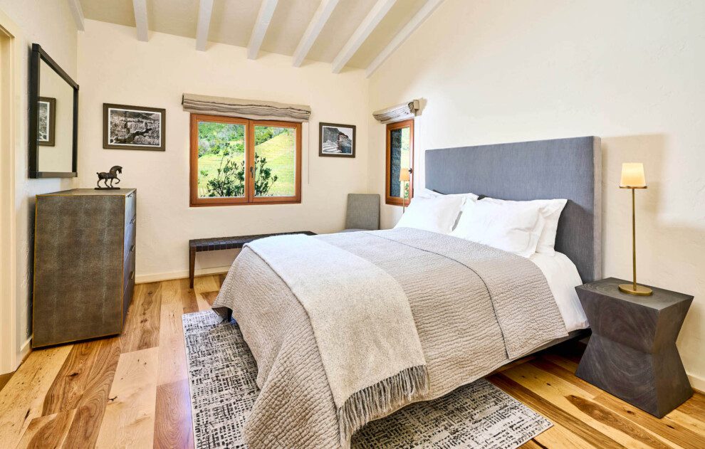 A cozy bed stands in a room with views out to vineyards